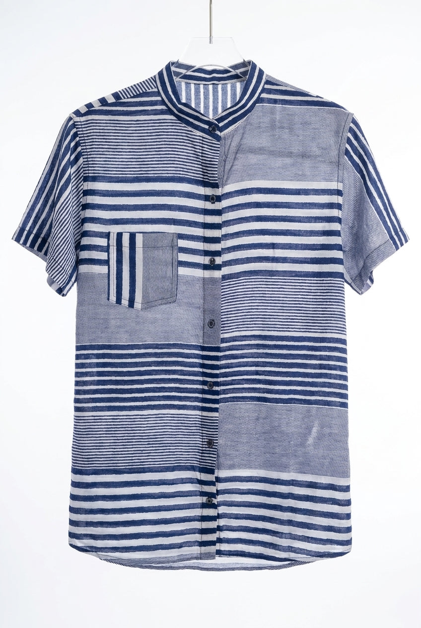 Camisa listrada azul e branca de mangas curtas, com gola, abertura frontal com botões e padronagem em blocos de listras horizontais e verticais. A peça aparece centralizada sobre fundo claro, em foto de produto para e-commerce.