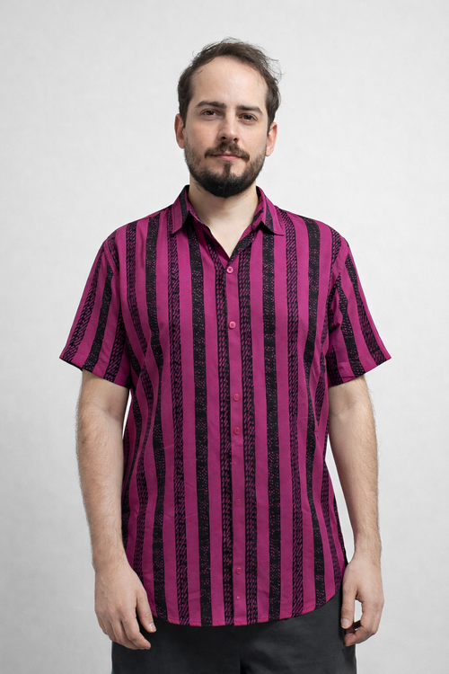 Pessoa em pé usando camisa de botão manga curta rosa pitaya com listras verticais pretas texturizadas, sobre fundo claro.