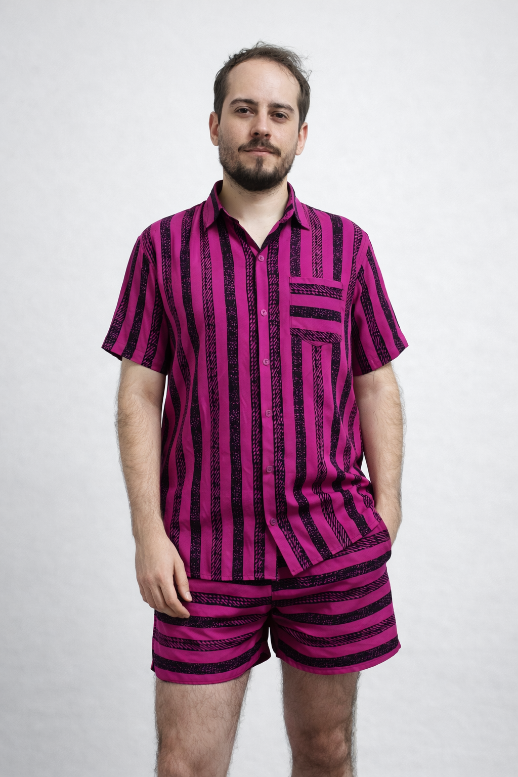 Pessoa usando conjunto listrado pitaya e preto com camisa de botão de manga curta e bermuda curta, em fundo neutro.